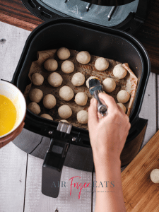 A home chef brushes the tops of the dough balls with melted butter before they are cooked in the air fryer.