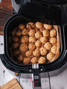 Cooked mozzarella bites in the bottom of an air fryer basket. They are golden brown and cooked perfectly.