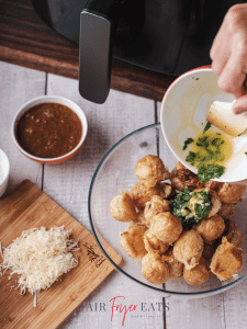 A home chef pours a mixture of melted butter and freshly-chopped parsley into a bowl with air fryer mozzarella bites.