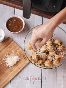 A home chef sprinkles freshly-grated parmesan cheese over warm mozzarella bites covered in butter and parsley.