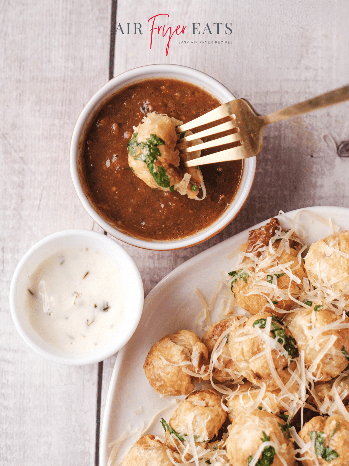 A fork holding a single air fryer mozzarella bite is dipped into a marinara dipping sauce. Nearby, there is a smaller bowl with ranch dipping sauce and a plate full of air fryer mozzarella bites covered with parmesan cheese and parsley.