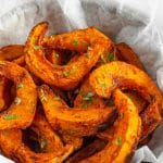 A wooden bowl is filled with bright orange, half-moon shaped pumpkin fries.