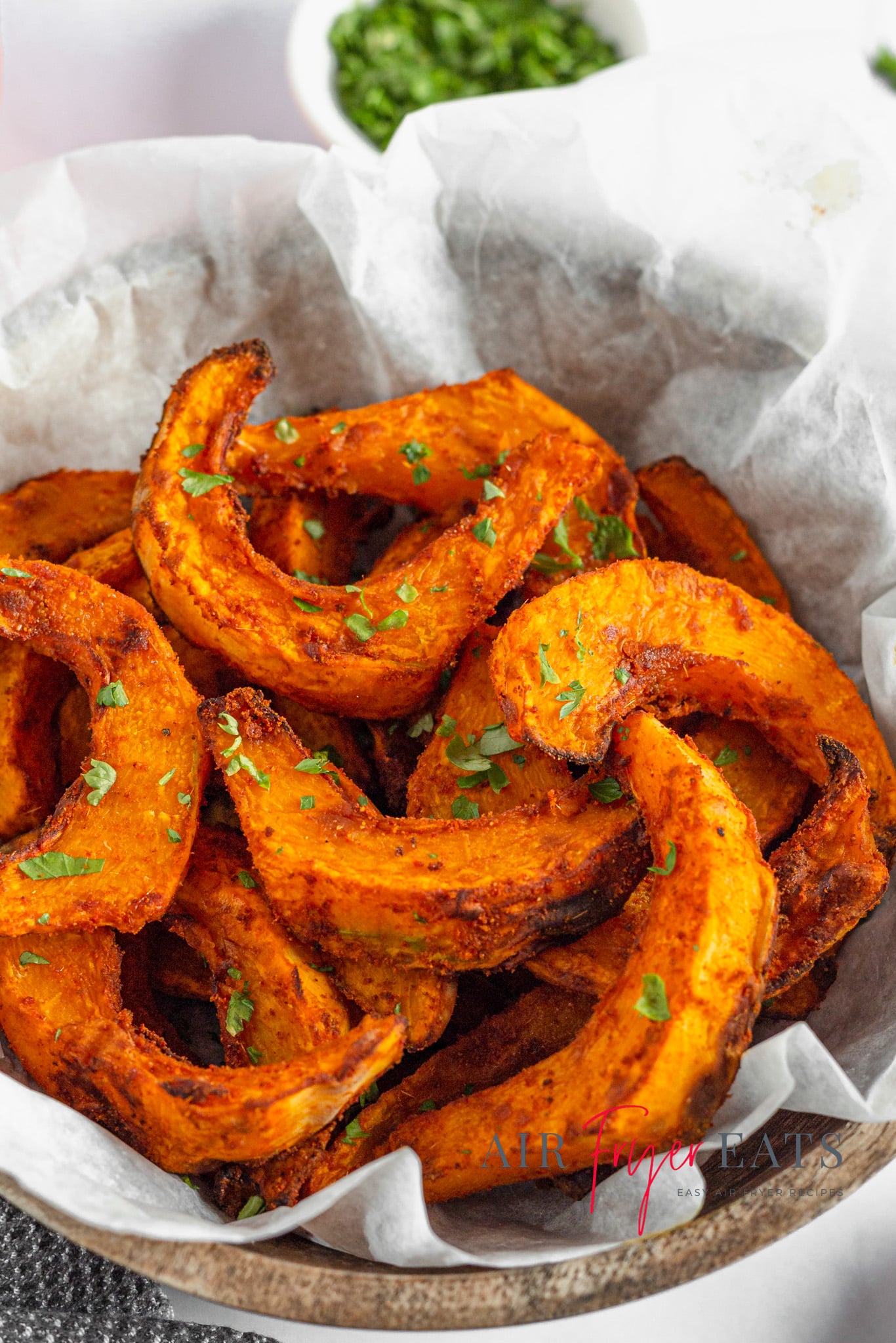 A wooden bowl is filled with bright orange, half-moon shaped pumpkin fries.